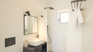 Casa de banho moderna com lavatório branco, um espelho grande, um chuveiro manual e um porta-toalhas.