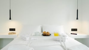 Cama bem arrumada com lençóis brancos, uma bandeja com muffins e um copo de suco de laranja, e um livro em uma mesinha de cabeceira.