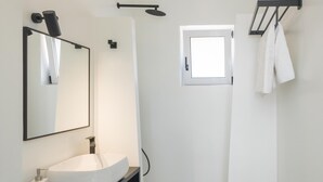 Um banheiro moderno com um espelho grande, uma pia branca, área de chuveiro e porta-toalhas.