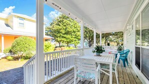 A covered porch with a wooden deck, white railings, and a table with chairs. - Remodeled & New to VRBO 2026! Crystal Beach,Community pool, 3 blocks to beach (Destin)