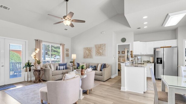 A spacious living area with a ceiling fan, a kitchen with white cabinets, and a dining area with a glass table. - Remodeled & New to VRBO 2026! Crystal Beach,Community pool, 3 blocks to beach (Destin)