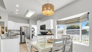 A modern kitchen with white cabinets, stainless steel appliances, and a glass dining table. - Remodeled & New to VRBO 2026! Crystal Beach,Community pool, 3 blocks to beach (Destin)