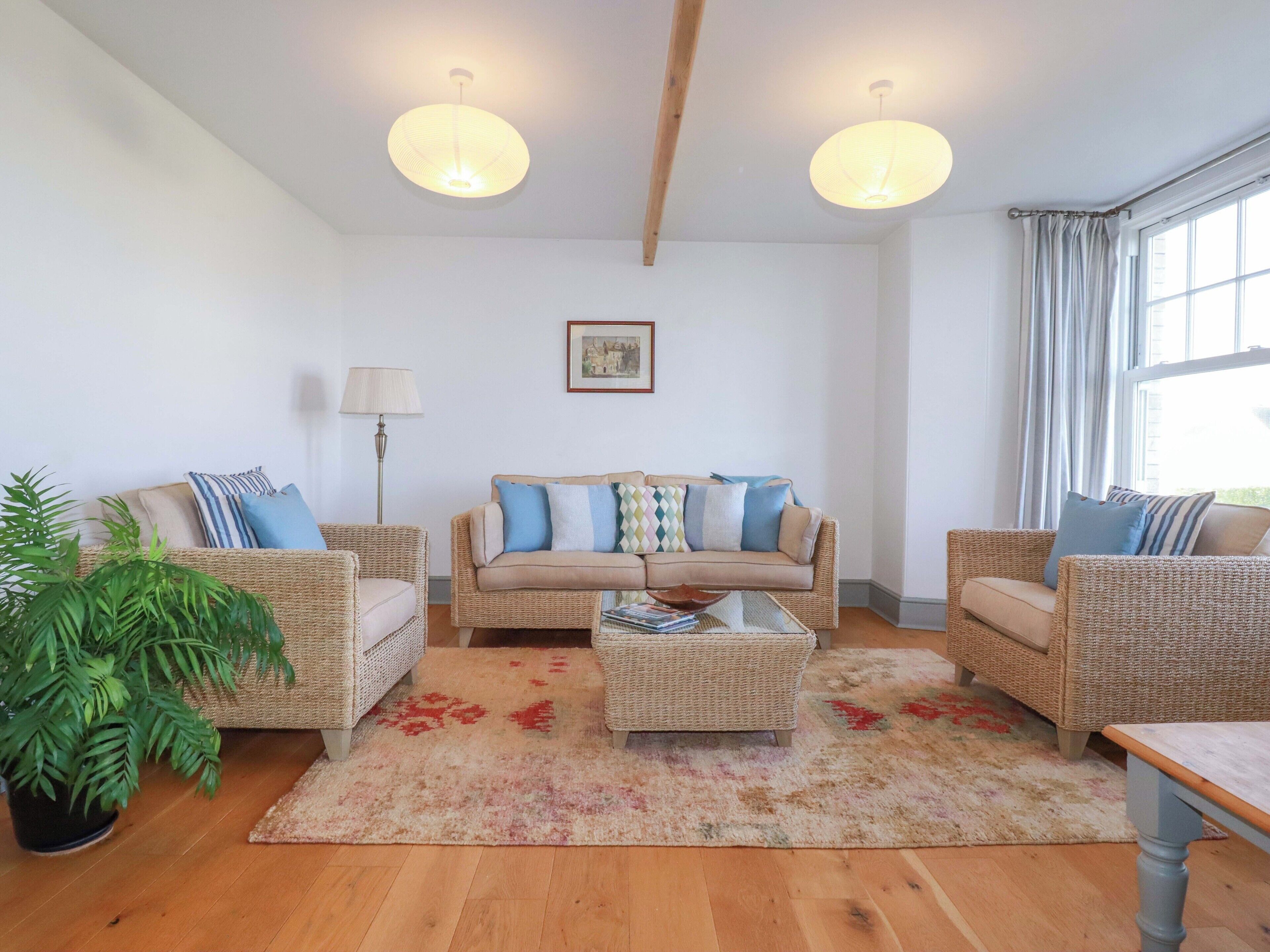 Una sala de estar con un sofá, dos sillones de mimbre, una mesa de centro, una lámpara de pie y una planta en maceta.