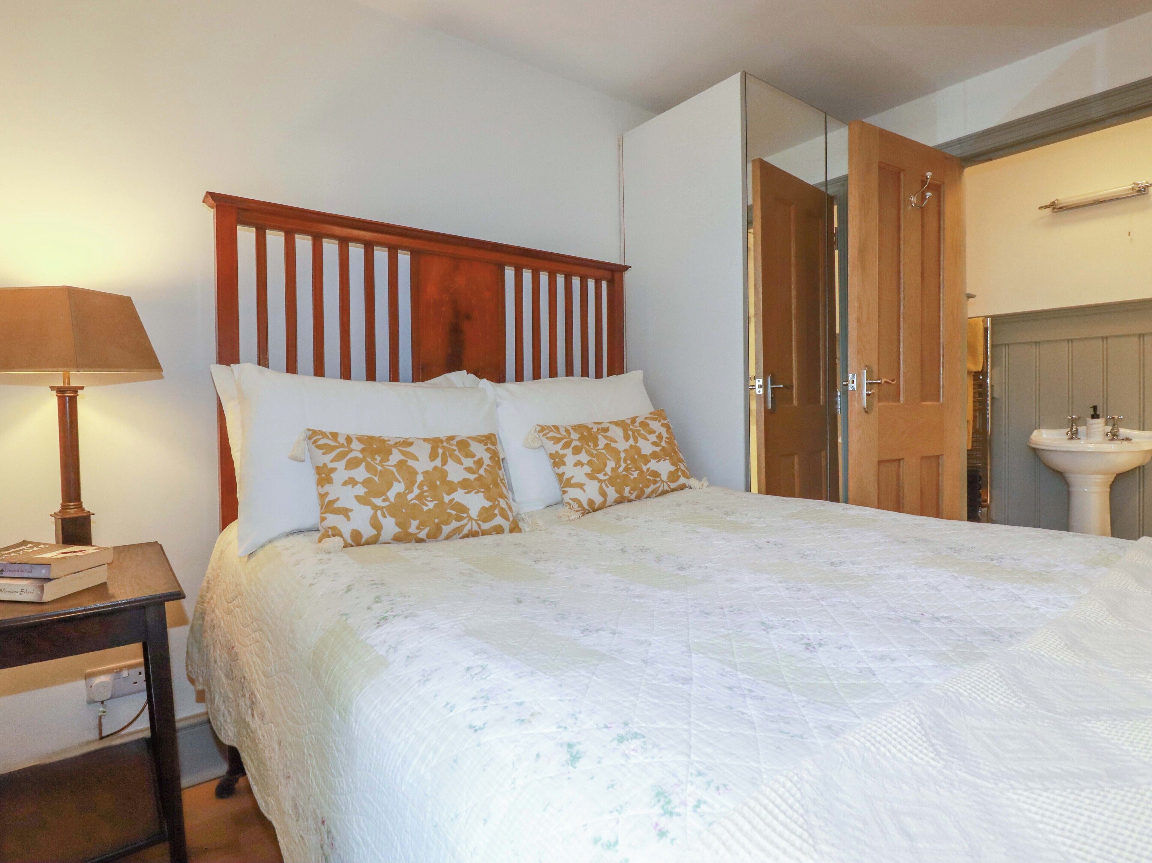 A neatly made bed with floral pillows, a bedside lamp, and a wooden headboard.