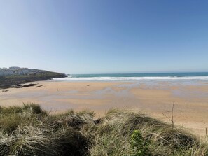 A beach with a clear sky, sandy shore, and grassy dunes. - Tradewinds (Newquay)
