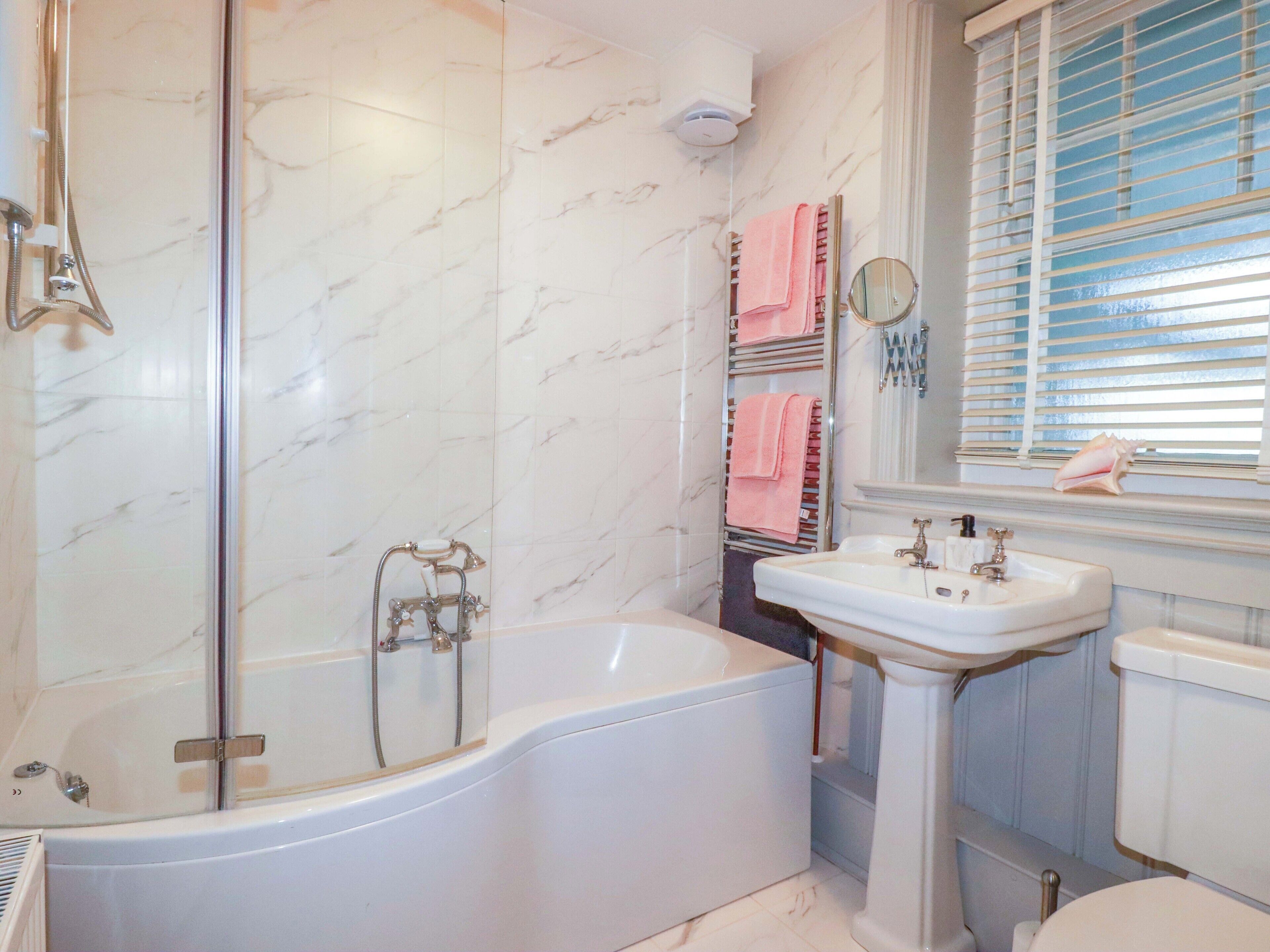 A bathroom with a bathtub, a sink, and a window with blinds.