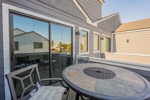 Une terrasse avec une table ronde et des chaises, de grandes portes-fenêtres coulissantes et une vue sur les maisons voisines.