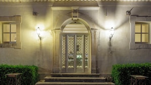 Un edificio con techo de tejas, una entrada central en arco y dos luces fijadas a la pared.