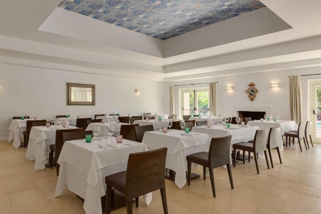 Un comedor con varias mesas y sillas, techo estampado y amplias ventanas.