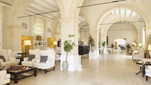 Un hall amplio con sofás blancos, un mostrador de recepción y plantas en macetas.