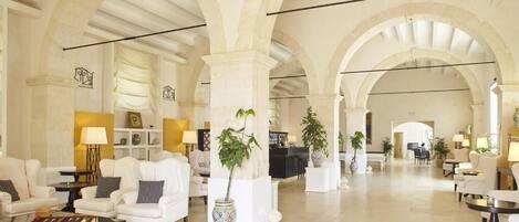 Een ruime lobby met witte banken, een receptiebalie en potplanten.