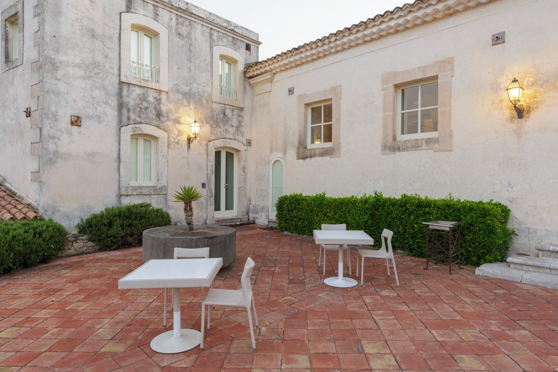 A courtyard with outdoor seating, a fountain, and a building with a tiled roof and light fixtures.