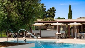 A pool area with a water feature, outdoor seating, and a covered bar area. - Hotiday Siracusa Floridia (Syracuse)