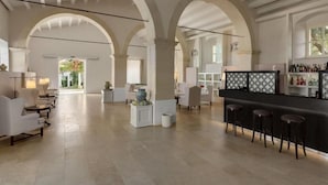 Un vestíbulo amplio con techos altos, columnas abovedadas, una zona de bar con taburetes y vistas al exterior.