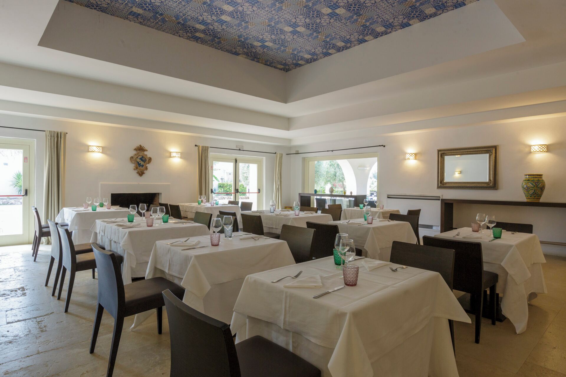 A dining area with multiple tables set for guests, featuring a patterned ceiling and natural light from windows.