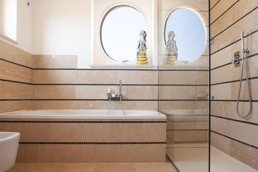 A bathroom with a large bathtub, a shower, and a toilet. There are two round windows above the bathtub.
