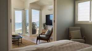 Een slaapkamer met een bed, een stoel, een televisie en uitzicht op de oceaan.