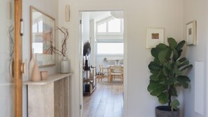 Een hal die leidt naar een eetruimte, met een grote plant, houten meubels en een spiegel aan de linkerkant.