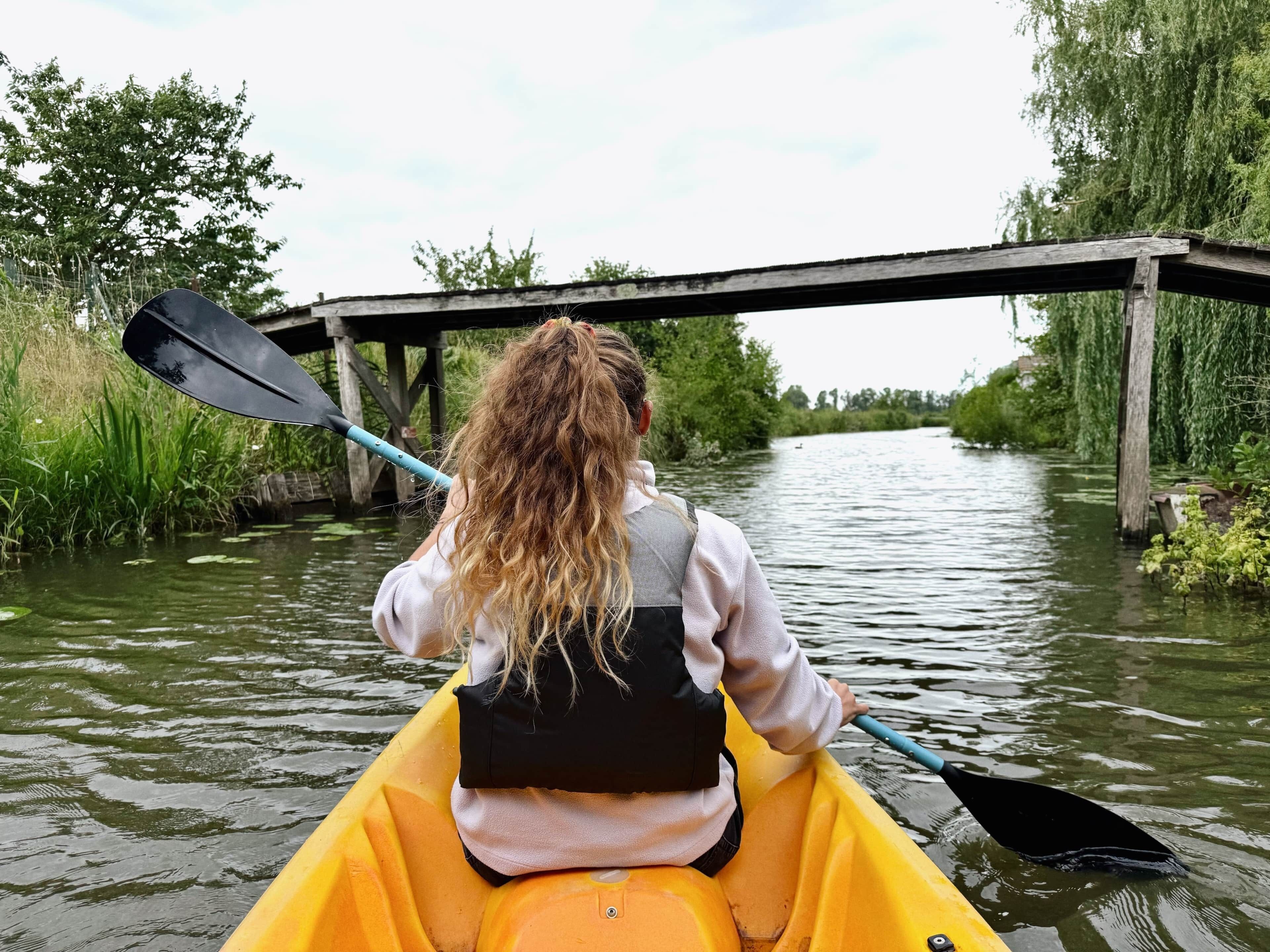 A person kayaking on a river with a bridge in the background.