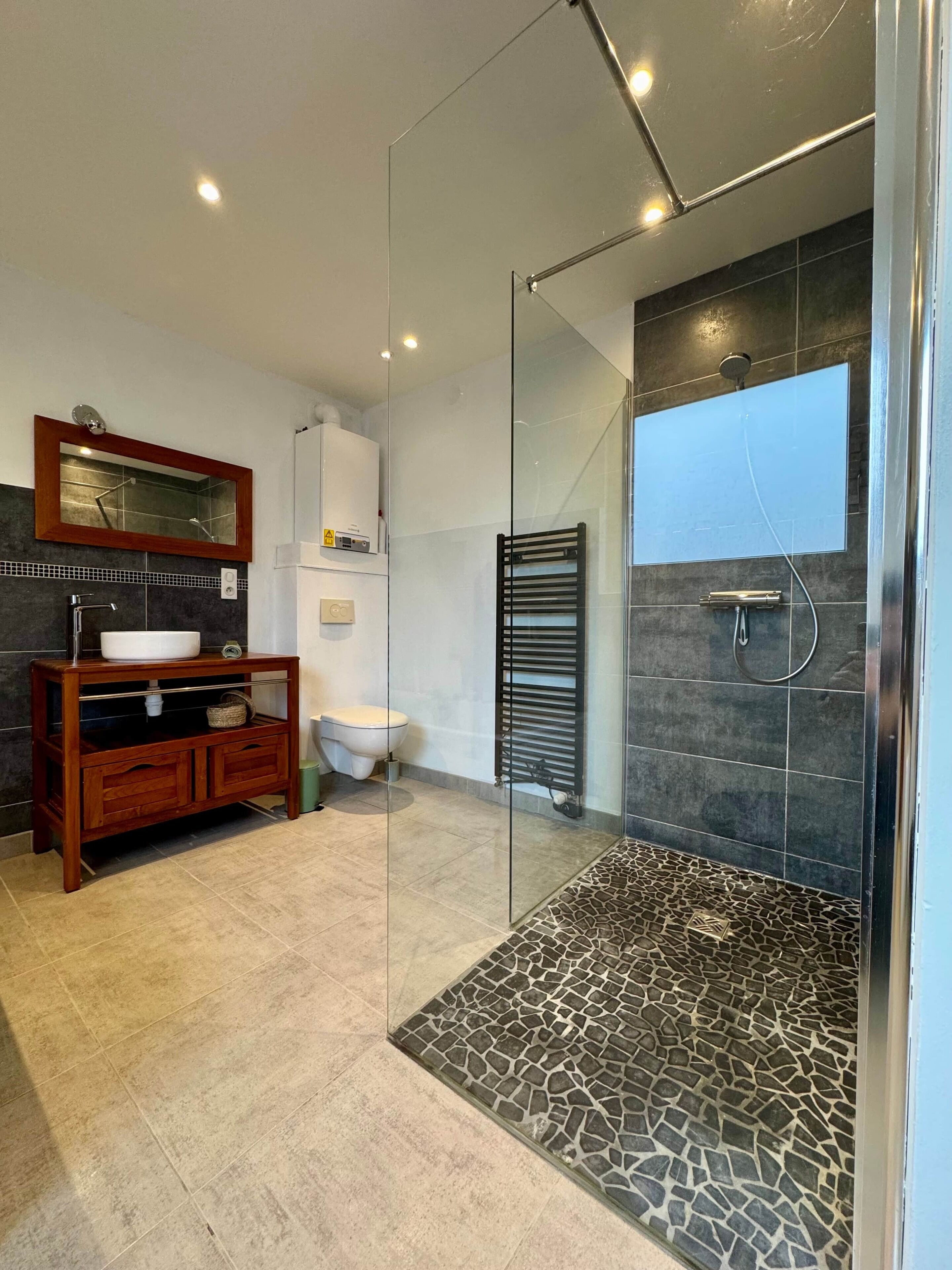 Une salle de bain moderne avec une douche à parois de verre, un meuble-lavabo en bois et un carrelage au sol.