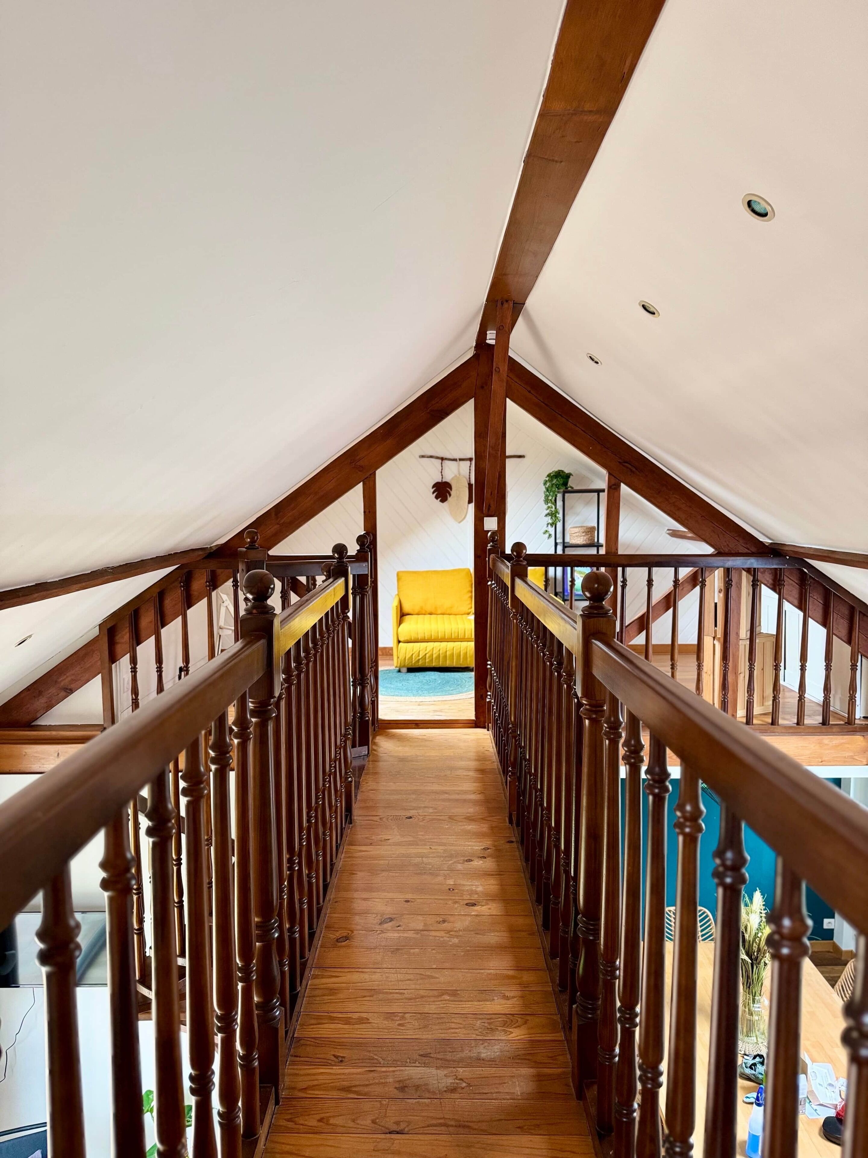 Una escalera de madera que conduce a una habitación con una silla amarilla y una planta.