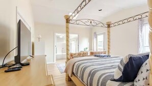 A bedroom with a four-poster bed, a bedside table with a TV, and a window with curtains. - Waterfront Escape with Pool Nature Lover Paradise (Stevensville)