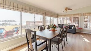 A dining area with a table and chairs, large windows with blinds, a ceiling fan, and a view of the beach. - Waterfront Escape with Pool Nature Lover Paradise (Stevensville)