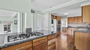 A modern kitchen with granite countertops, wooden cabinets, and a central island with a stove. - Waterfront Escape with Pool Nature Lover Paradise (Stevensville)