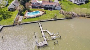 An aerial view of a residential area with a large house featuring a swimming pool, dock, and surrounding greenery. - Waterfront Escape with Pool Nature Lover Paradise (Stevensville)
