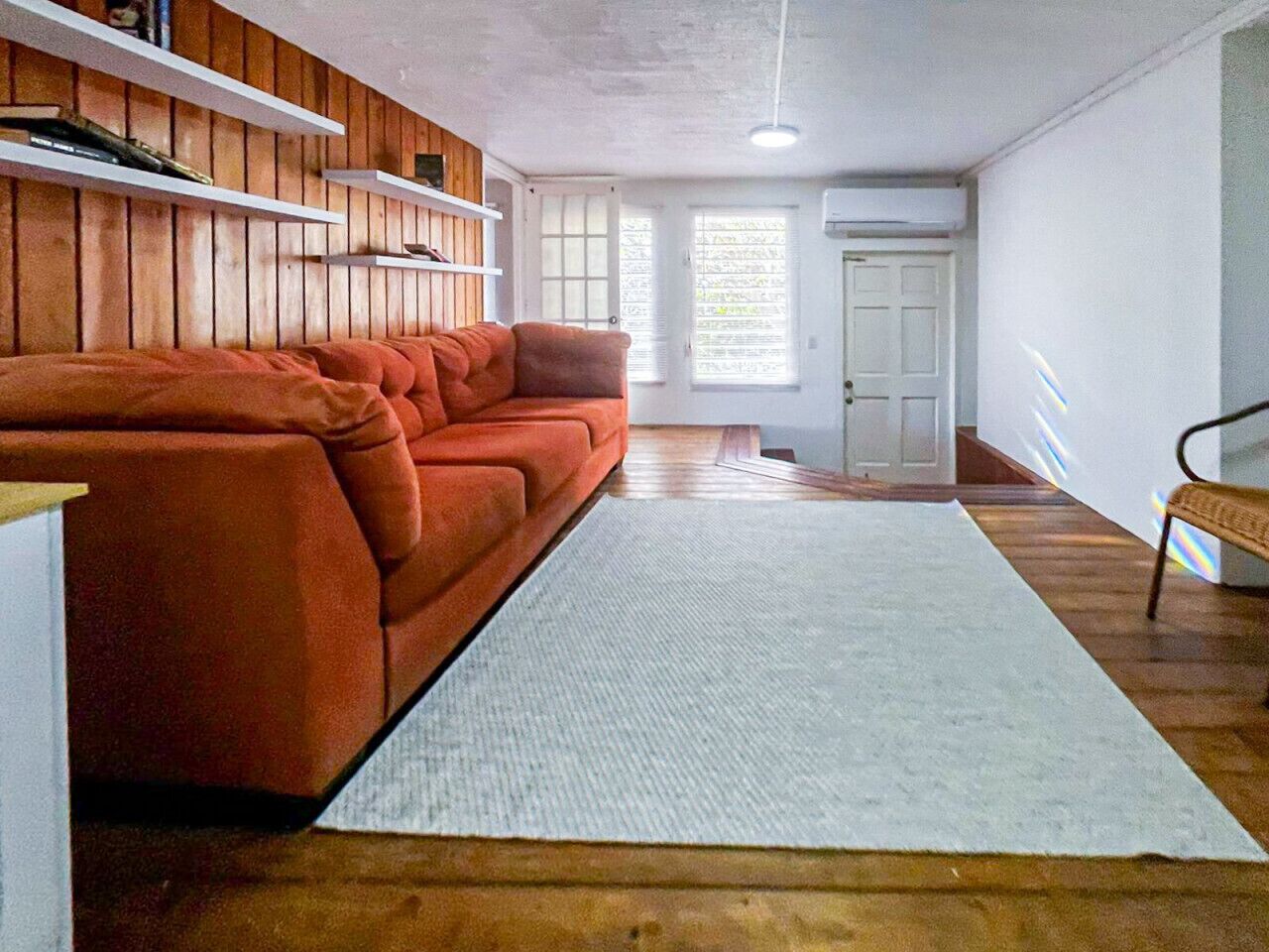 A room with a sofa, a rug, wooden walls, a door, and a bench.