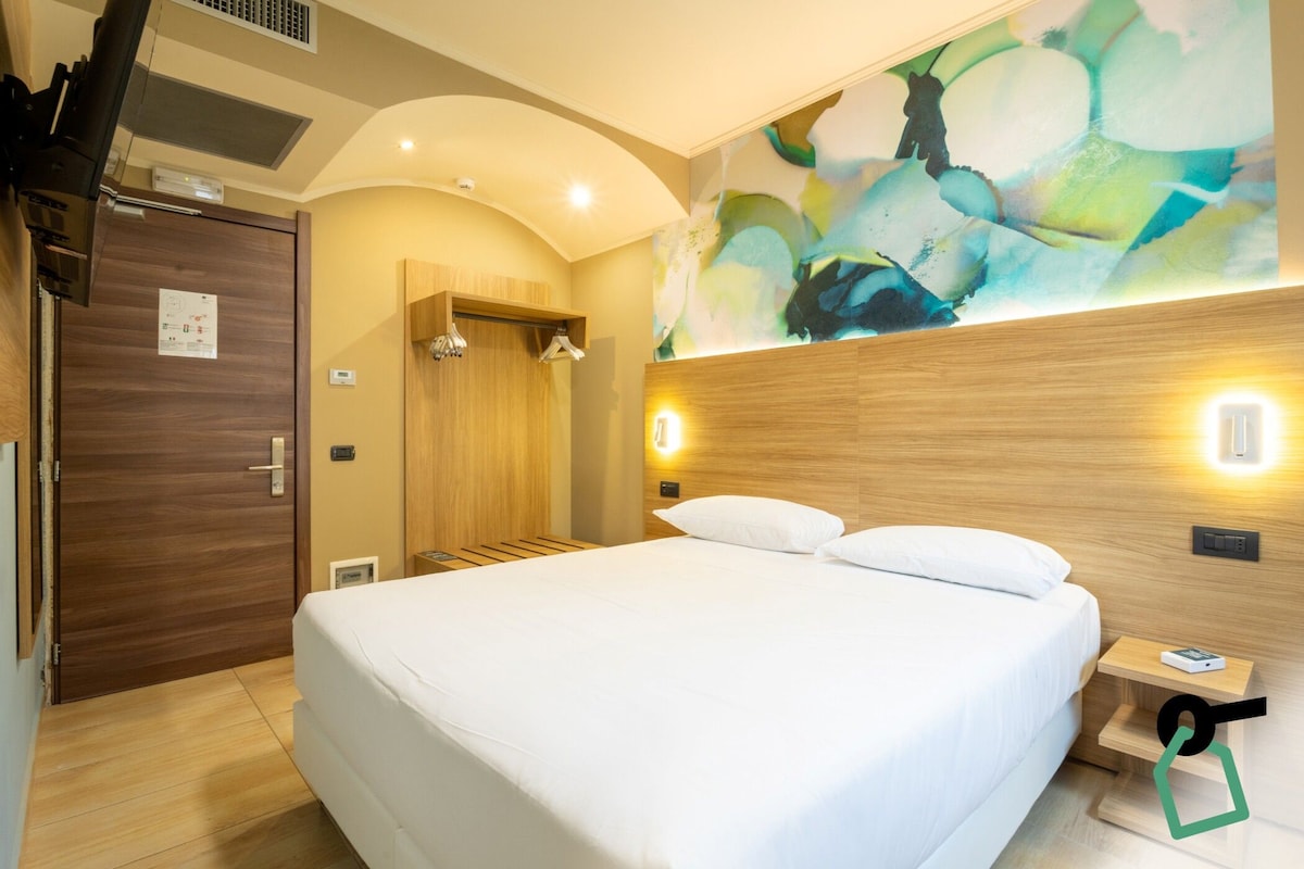Une chambre d’hôtel avec un grand lit, une tête de lit en bois, une lampe fixée au mur et un tableau.