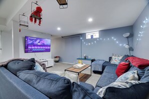 A modern living room with a flat-screen TV, a sofa, a coffee table, and a desk with a lamp. - The Poconos Fun Chalet w/Game Room (Tobyhanna)