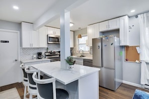 A modern kitchen with white cabinets, a stainless steel refrigerator, a built-in oven, and a central island with bar stools. - The Poconos Fun Chalet w/Game Room (Tobyhanna)