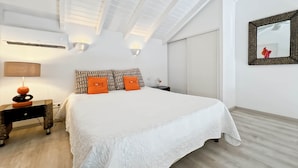 A bedroom with a skylight, a bed with patterned pillows, a bedside table with a lamp, and a mirror on the wall. - Mango Orange duplex with pool in Orient Bay! (Orient bay)