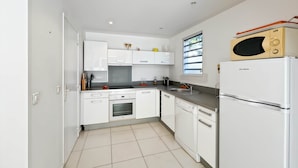 A modern kitchen with white cabinets, a built-in oven, a dishwasher, and a microwave on top of a refrigerator. - Mango Orange duplex with pool in Orient Bay! (Orient bay)