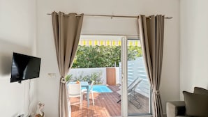A modern living room with a flat-screen TV, a sofa, a coffee table, and a view of an outdoor pool area. - Mango Orange duplex with pool in Orient Bay! (Orient bay)