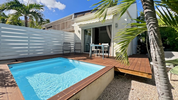 A swimming pool with a wooden deck, a white fence, and a patio area with chairs and a table. - Mango Orange duplex with pool in Orient Bay! (Orient bay)