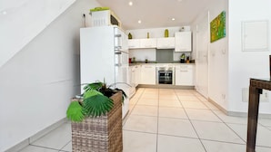 A modern kitchen with white cabinets, a built-in oven, and a small dining area with a wicker basket and potted plant. - Mango Vert duplex with pool in Orient Bay! (Orient bay)