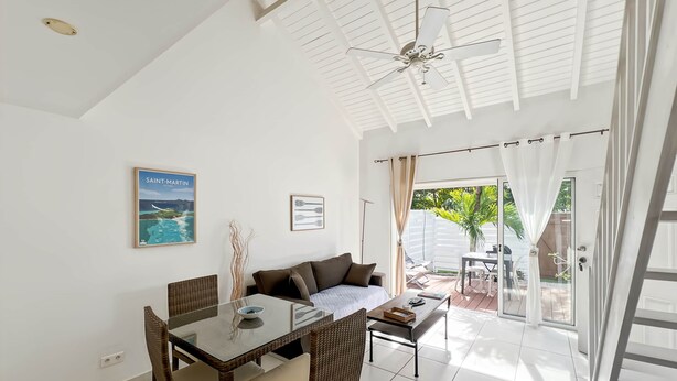 A modern living room with a dining area, a ceiling fan, and a view of the outdoor patio. - Mango Vert duplex with pool in Orient Bay! (Orient bay)