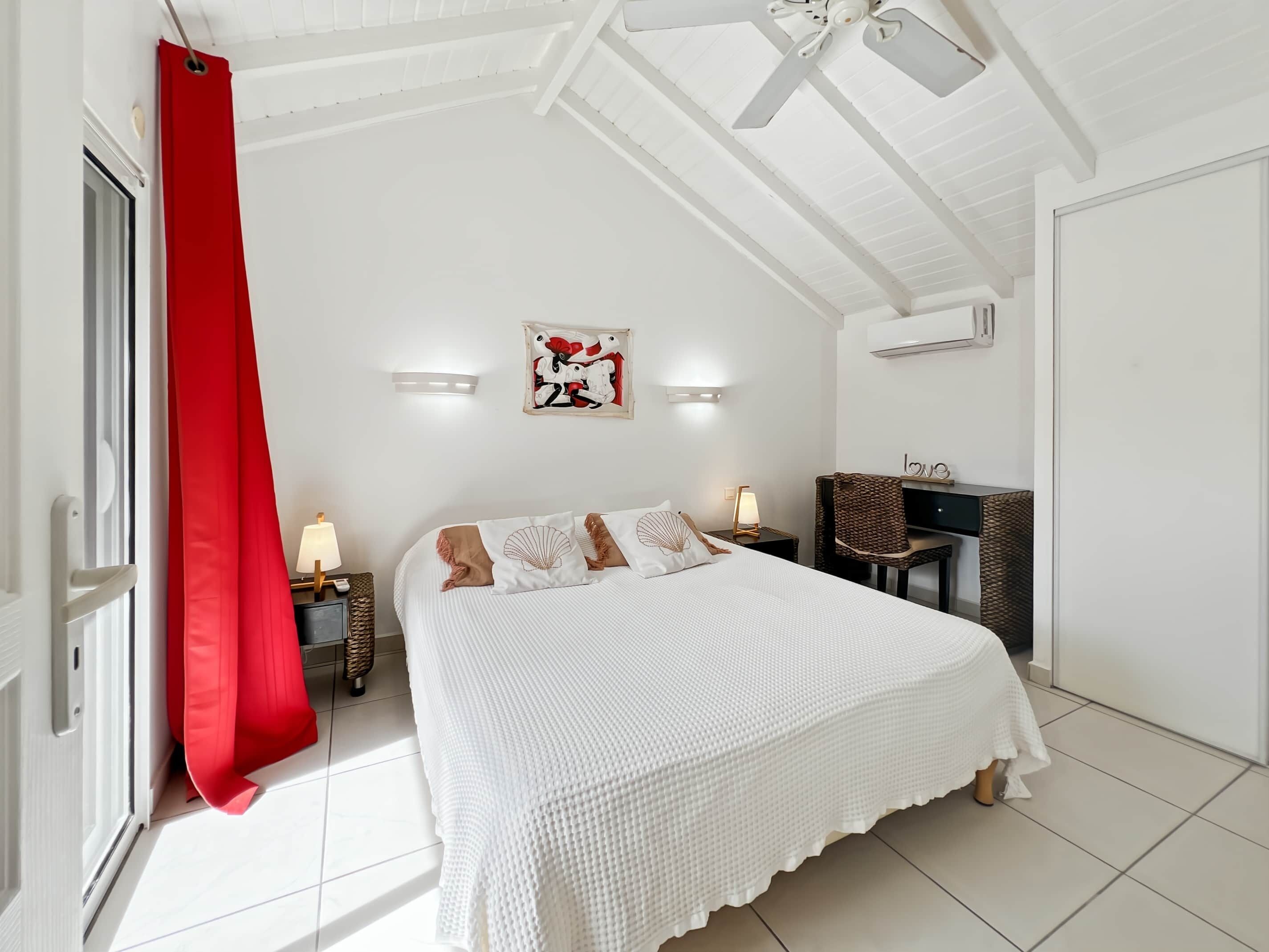 A bedroom with a bed, a desk, a chair, a red curtain, and a ceiling fan.