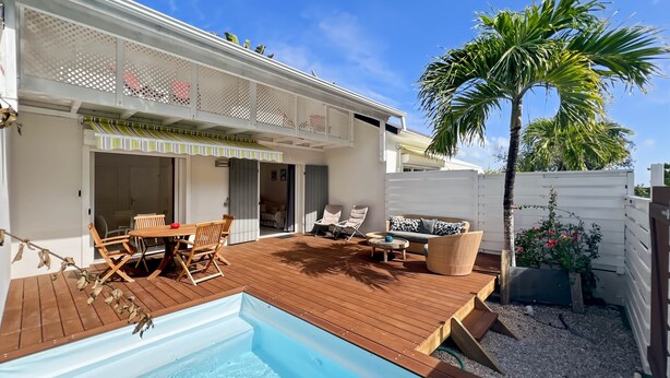 Un jardin avec une piscine, une terrasse en bois, du mobilier d’extérieur et un palmier.