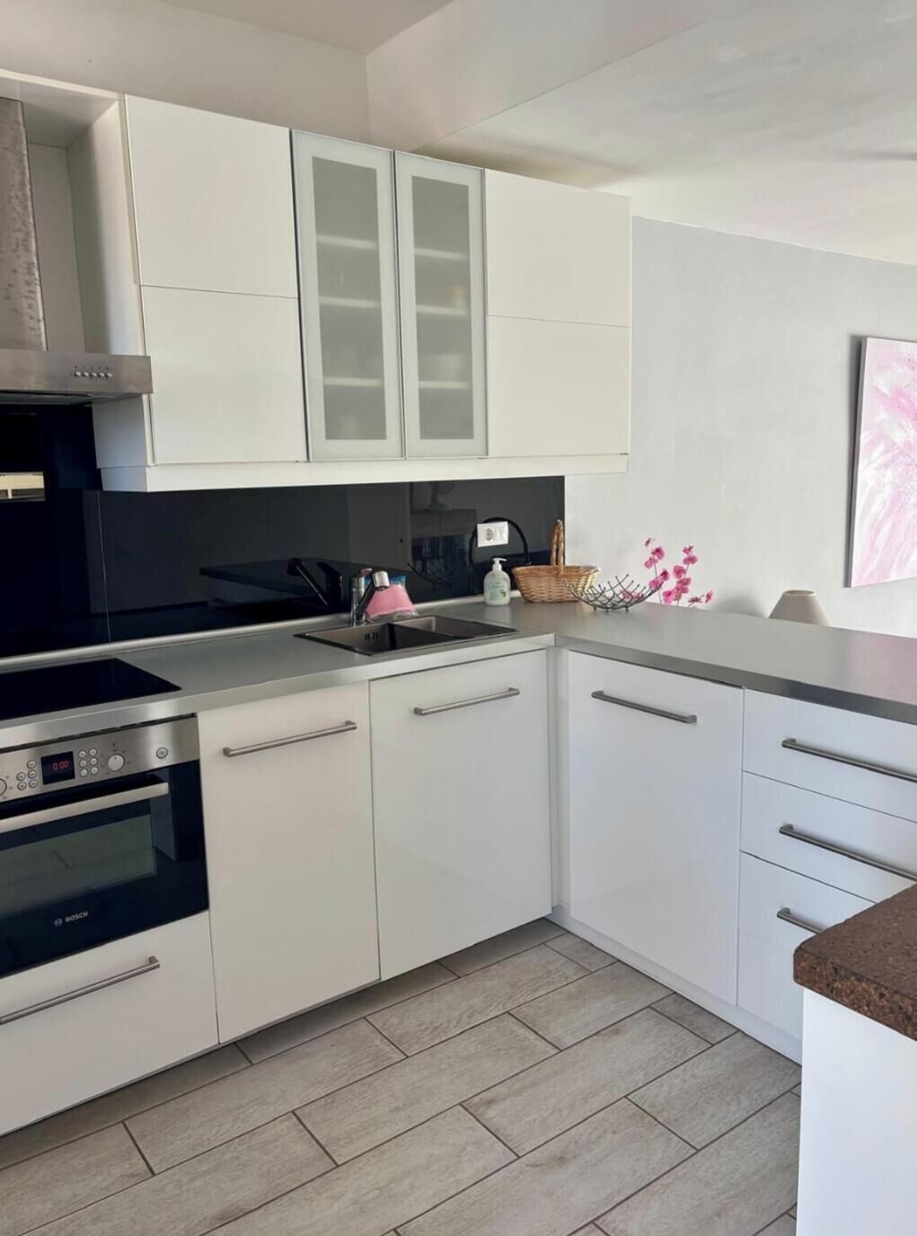 Una cocina moderna con armarios blancos, un horno Bosch, una campana extractora de acero inoxidable y una encimera de granito.