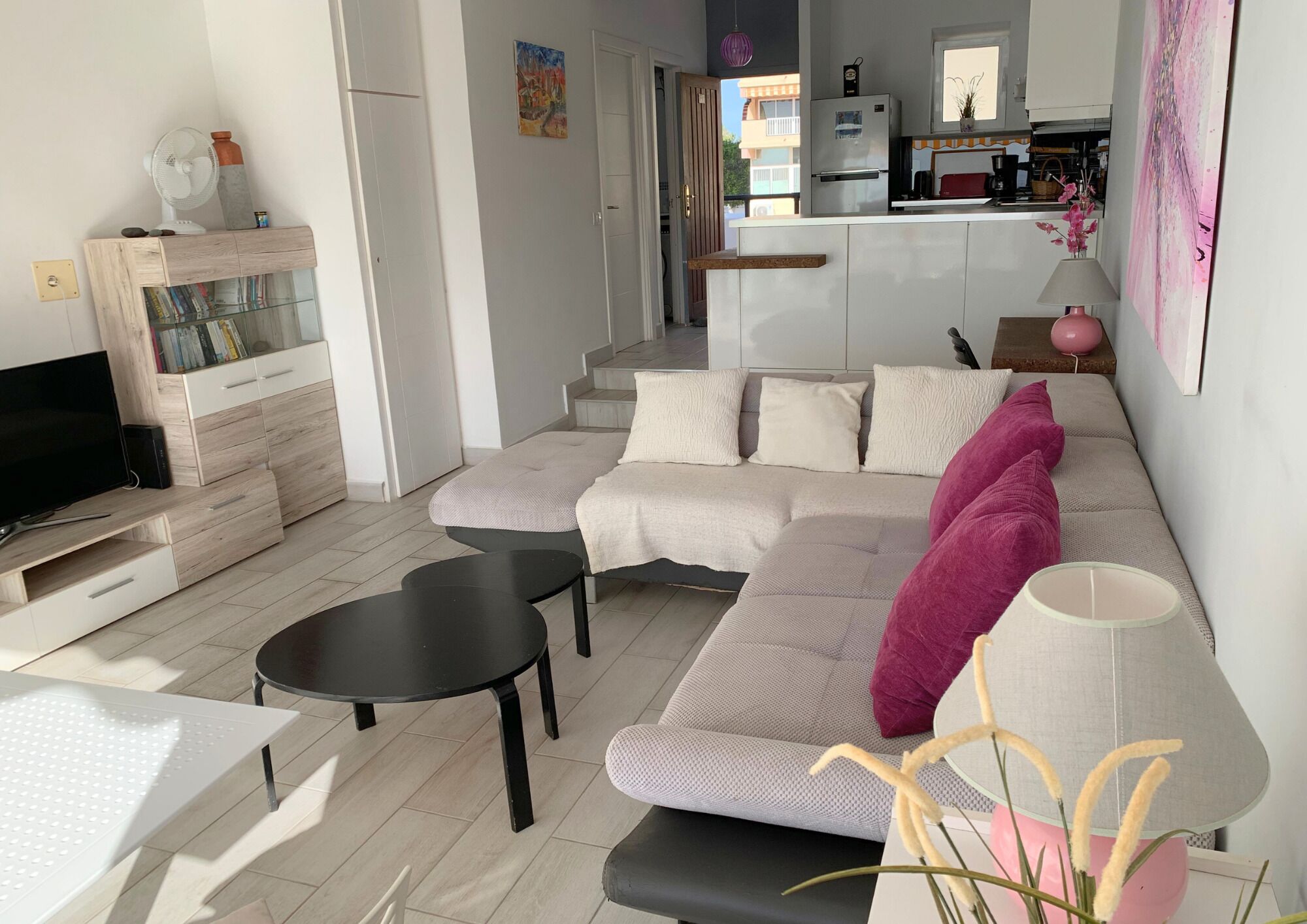Una sala de estar moderna con un sofá modular, un televisor de pantalla plana, una mesa de centro y un comedor con una mesa y sillas.