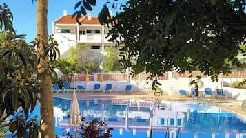Zona de piscina con sillas de descanso y un edificio al fondo.