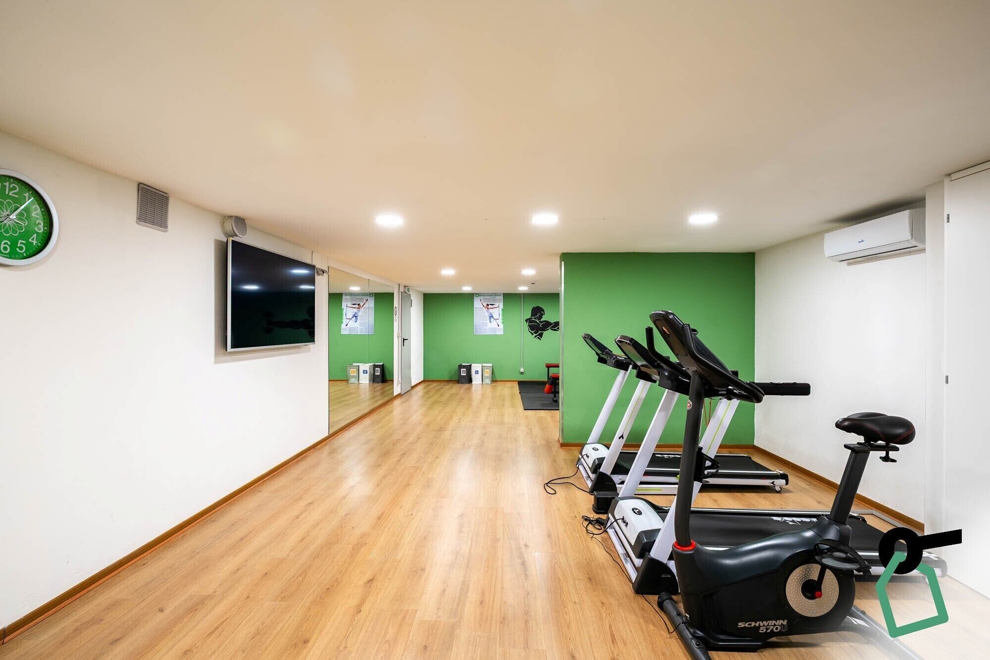 A gym with exercise equipment, a clock, and green walls.