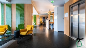 A modern hotel lobby with a reception desk, two yellow chairs, a glass table, and a green wall with vertical gardens. - Hotiday Firenze Peretola (Florence)