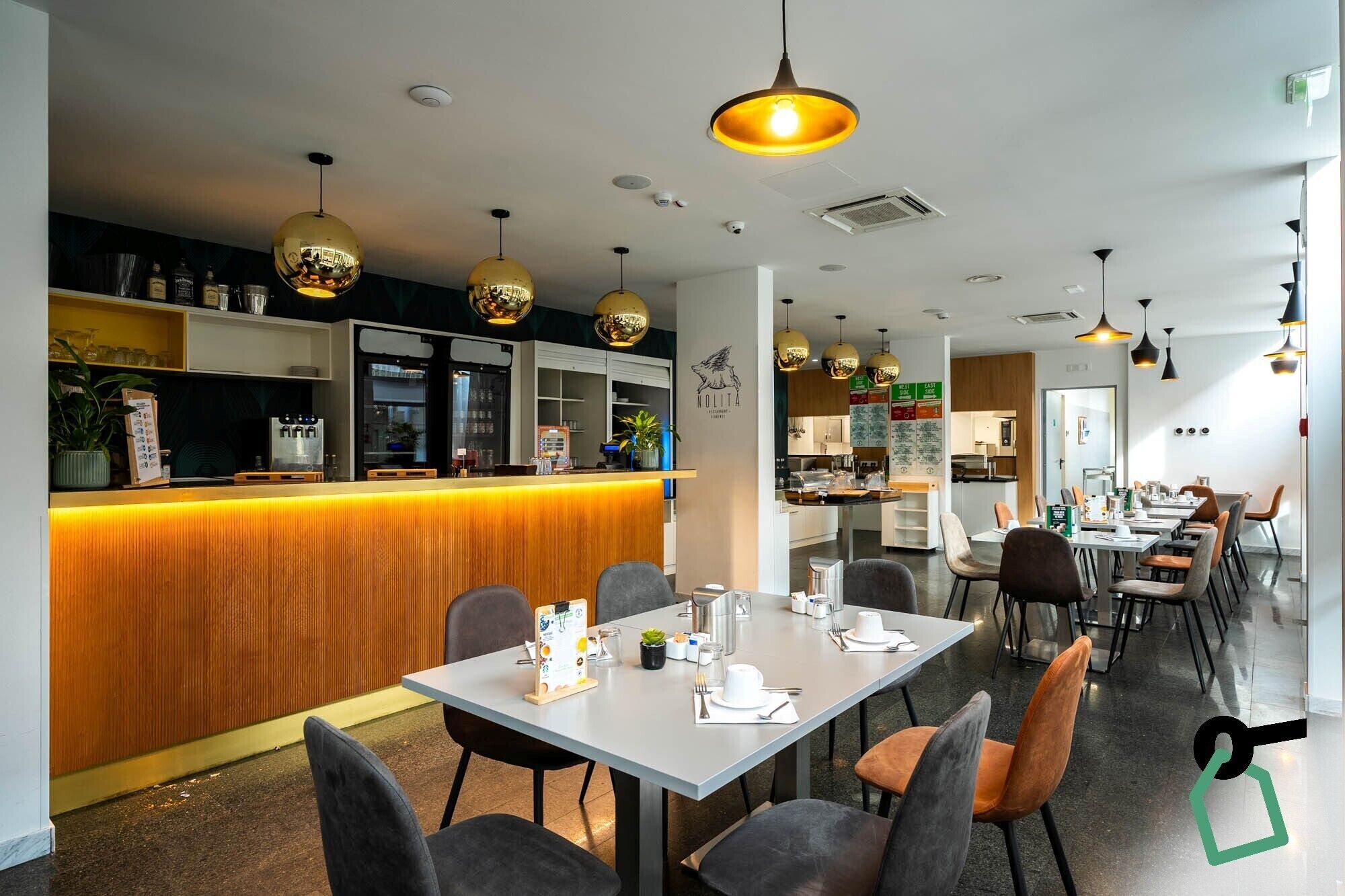 A modern restaurant interior with a wooden bar, multiple dining tables, and pendant lighting.