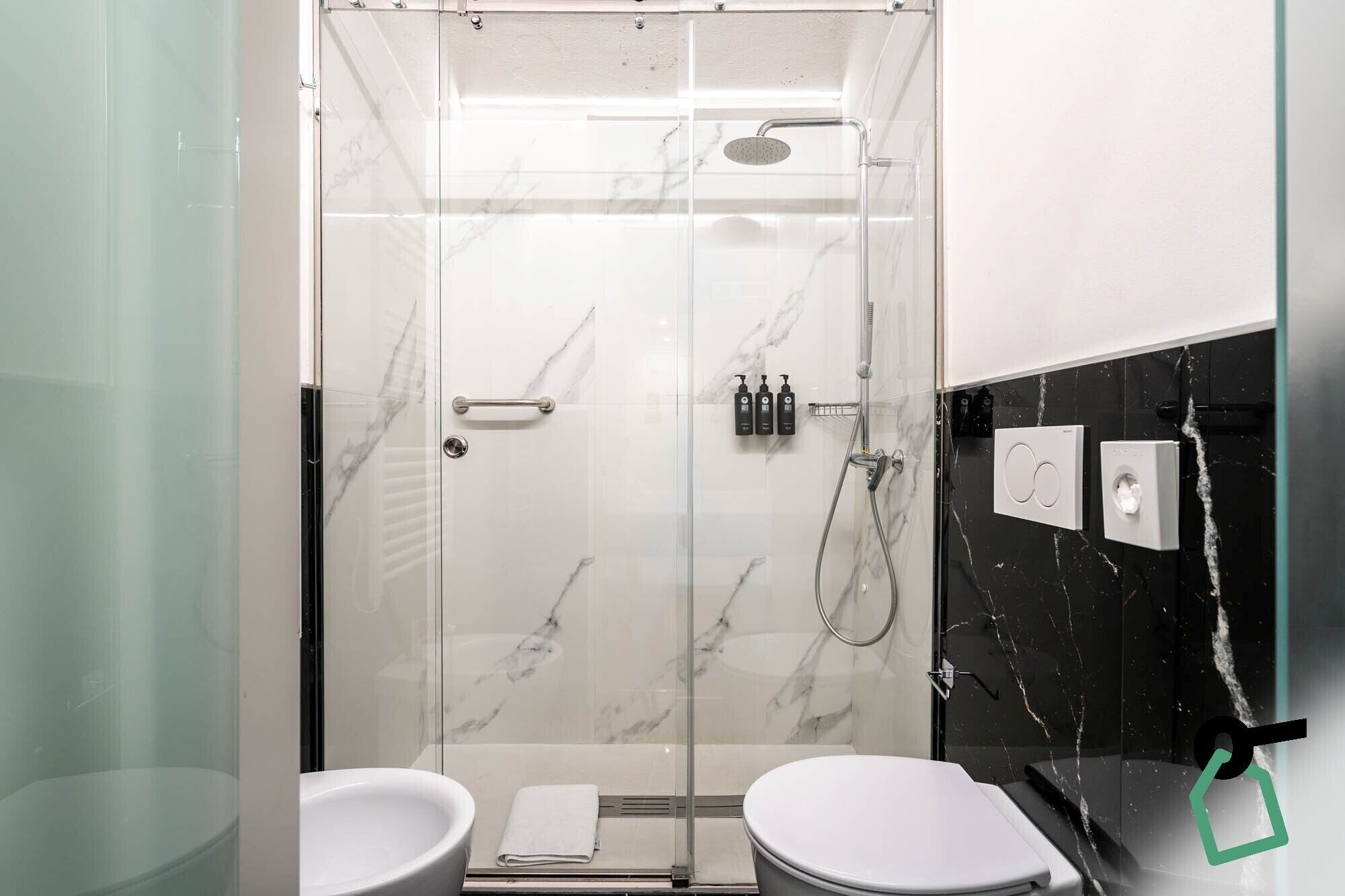 Een moderne badkamer met een douche met glazen wand, witte marmeren wanden en een accentmuur van zwart marmer.