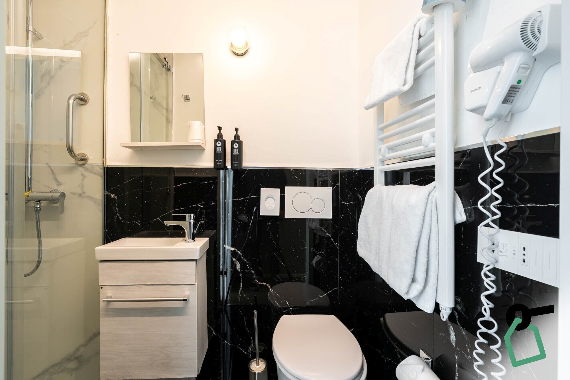 A modern bathroom with a glass shower enclosure, a white sink, a black marble backsplash, a toilet, and a towel rack with a hairdryer.