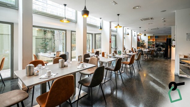 A modern restaurant with long tables, chairs, and pendant lighting. - Hotiday Firenze Peretola (Florence)